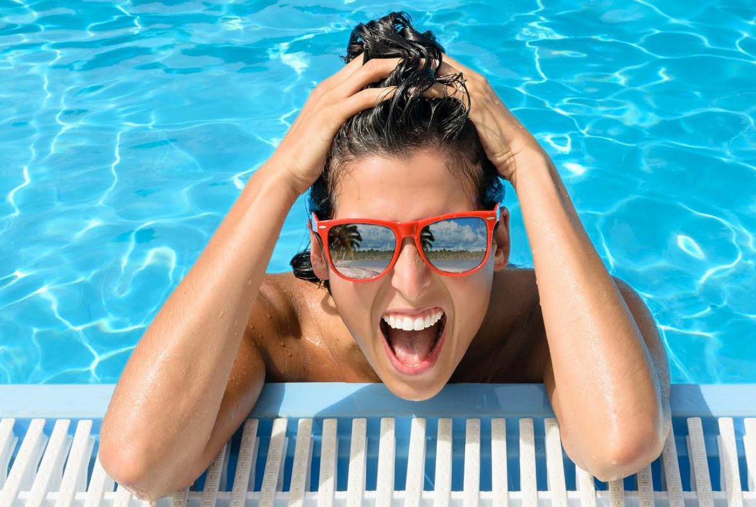 Happy woman in swimming pool wearing sunglasses.