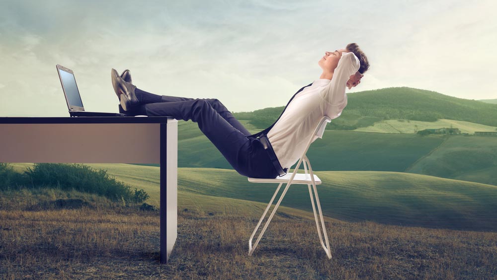 Young businessman relaxing at his desk in the middle of a green meadow.