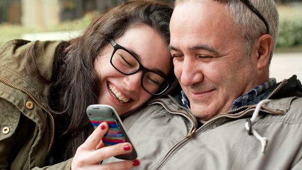 Father and daughter look at phone smiling and happy