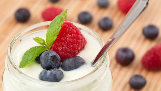 A jar of yogurt with berries and a spoon.