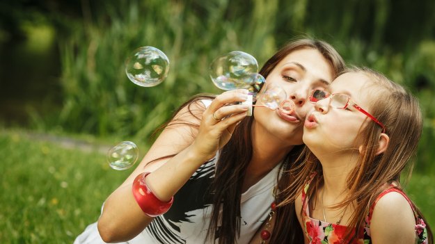 Happy mom and daughter blowing bubbles outside.