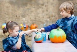 Two kids painting a pumpkin.