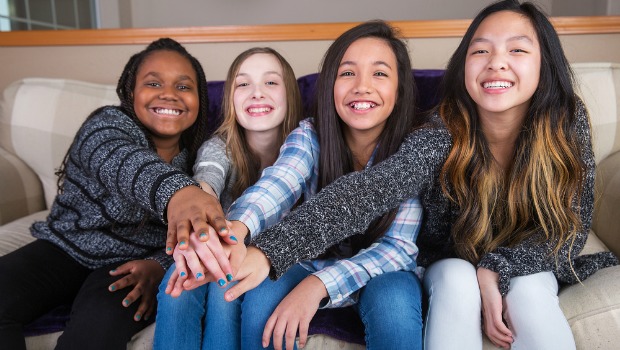 Diverse group of teen girls sitting on a couch touching hands.