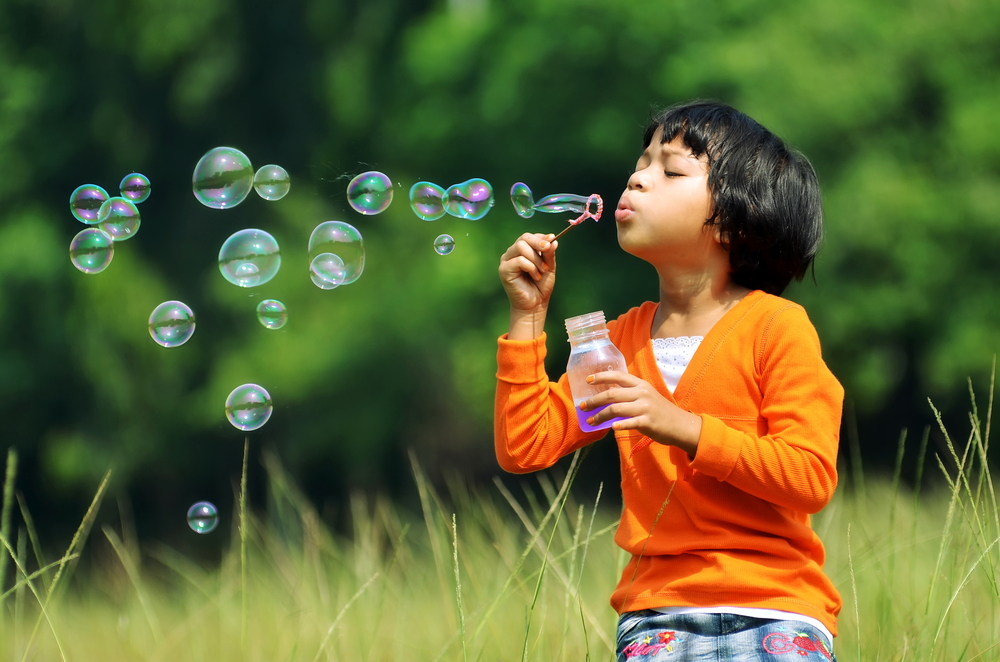 Children playing with soap bubbles on a green environment background