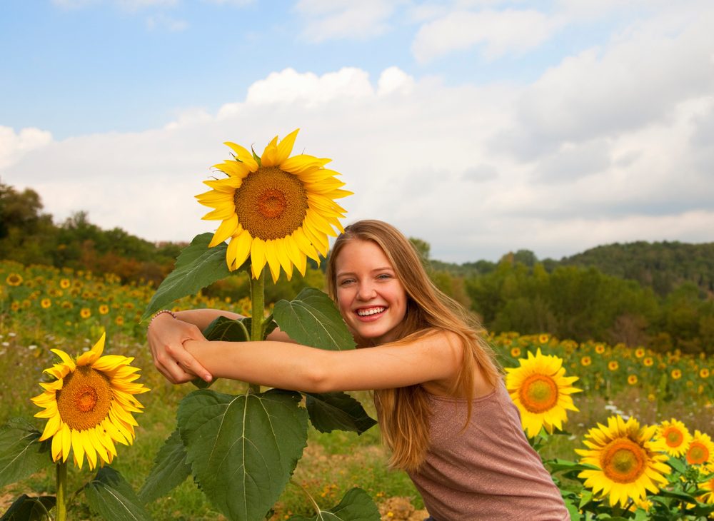 Teenage girl hugging sunflower in field