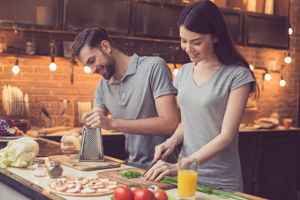 Pizza time. Young beautiful couple in kitchen. Family of two preparing food. Couple making delicious pizza. Man grating cheese. Nice loft interior with light bulbs