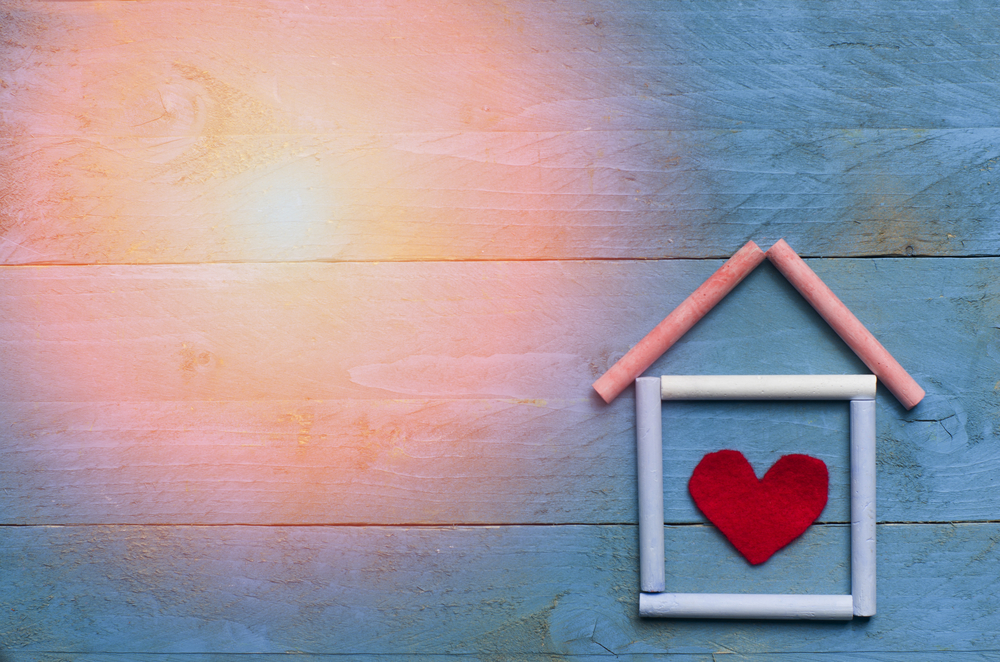 House made of chalk with red heart in on blue wooden background. Sun in a corner
