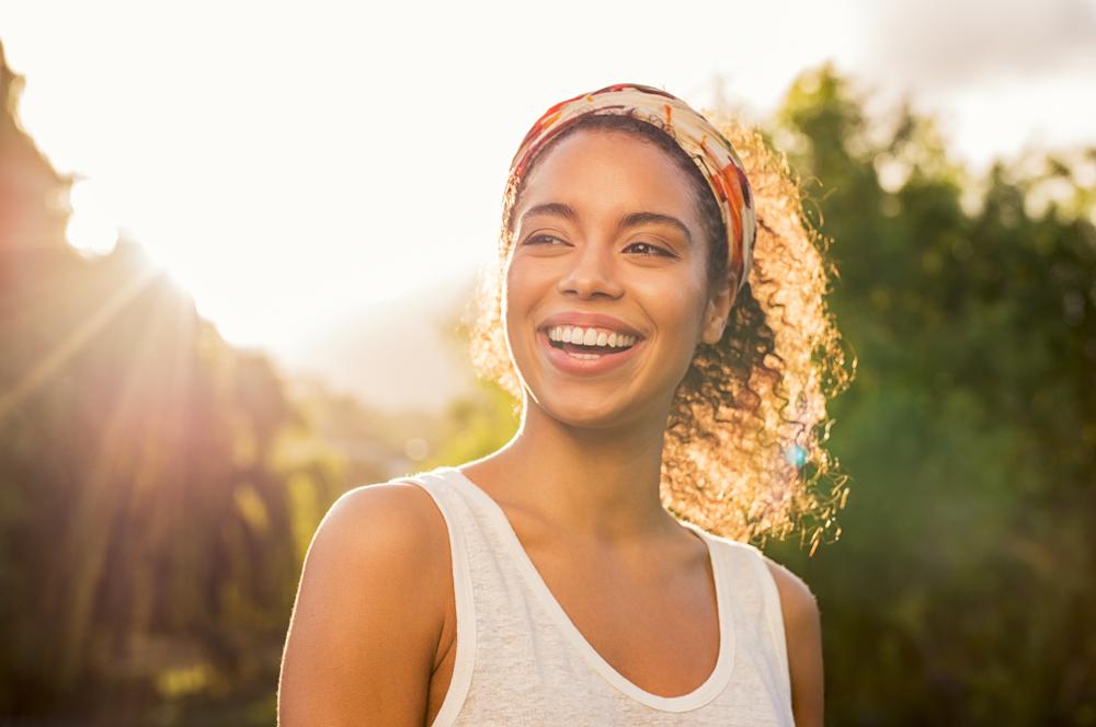 Portrait of beautiful african american woman smiling and looking away at park during sunset.