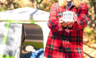 Woman camping in plaid shirt with coffee mug.