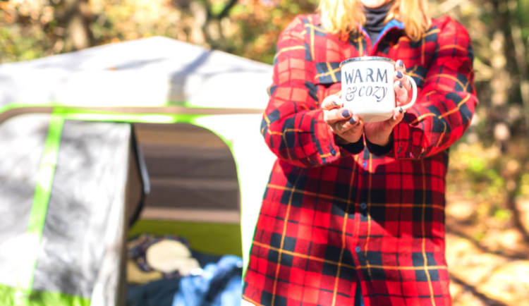 Woman camping in plaid shirt with coffee mug.