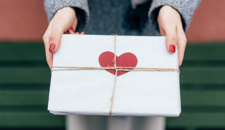 Woman giving present wrapped in white paper with red heart