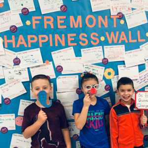 A group of children standing in front of their School Happiness Wall.