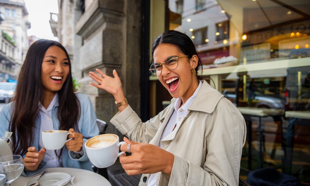 Two young women laughing and drinking coffee.